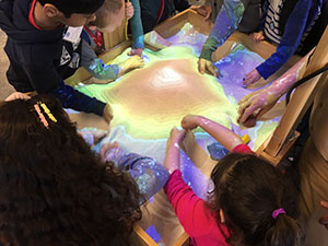 Kids move sand to form topographic features in the interactive sandbox.
