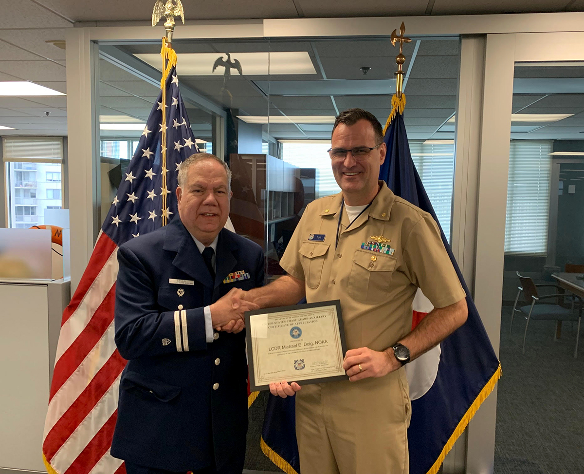 An image of Hiram Escabi presenting LCDR Michael Doig with a coin and certificate for outstanding cooperation and assistance from the US Coast Guard Auxiliary.