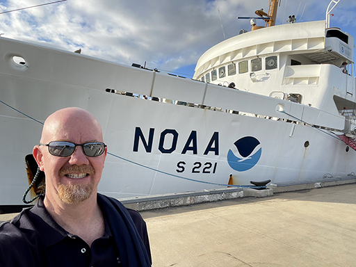 An image of Darren Wright taken in Pearl Harbor, Hawaii, with NOAA Ship Rainier in the background.