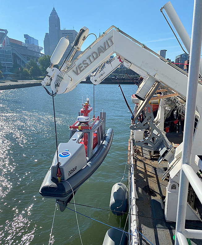 An image showing the uncrewed surface vessel, DriX, being lifted by the davits of NOAA Ship Thomas Jefferson in Cleveland, Ohio.