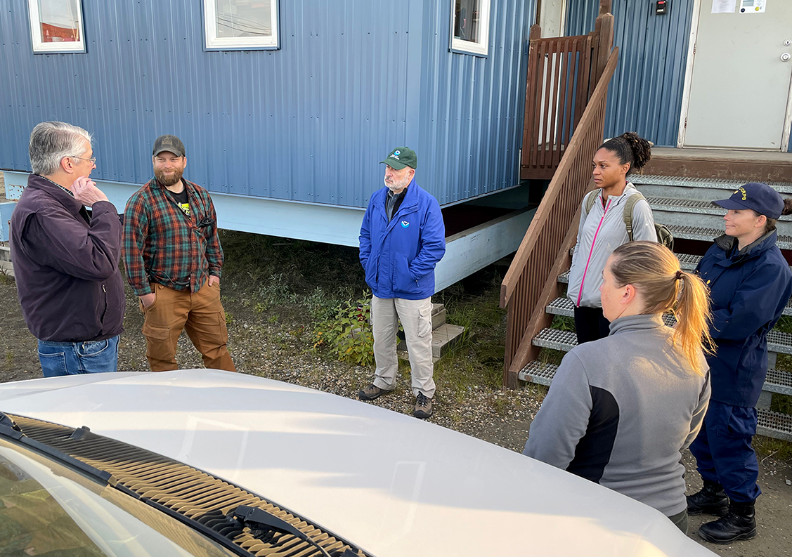 An image depicting a meeting with, from left to right, Nome City Manager Glenn Steckman, Port of Nome Harbormaster Lucas Stotts, Dr. Richard Spinrad, Dr. Letise LaFeir, LCDR Hadely Owen, and Dr. Kelly Kryc.