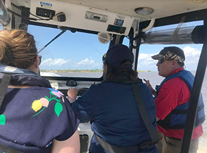 An image showing the harbormaster's cockpit with Julia Powell looking on as CDR Briana Hillstrom drives the harbormaster vessel through the Port of Mobile, Alabama.