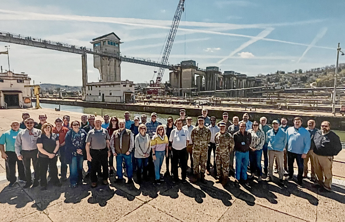 A group image of attendees at the Inland Waterways Users Board meeting with the Monongahela River and Charleroi Lock and Dam 4 in the background.