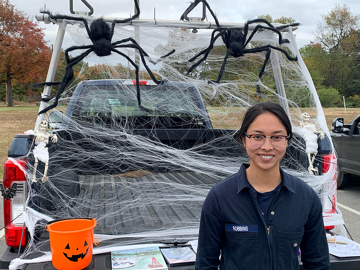 LTJG Carly Robbins in front of Bay Hydro II's trunk or treat display at Naval Air Station Patuxent River.