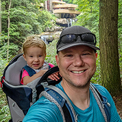 Mark Van Waes carrying his daughter in a backpack with Frank Lloyd Wright's Falling Water in the background.