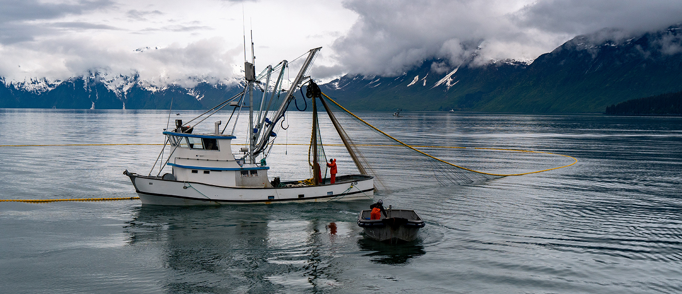 An image of a fishing boat with deployed fish net in calm water with mountains in the background.